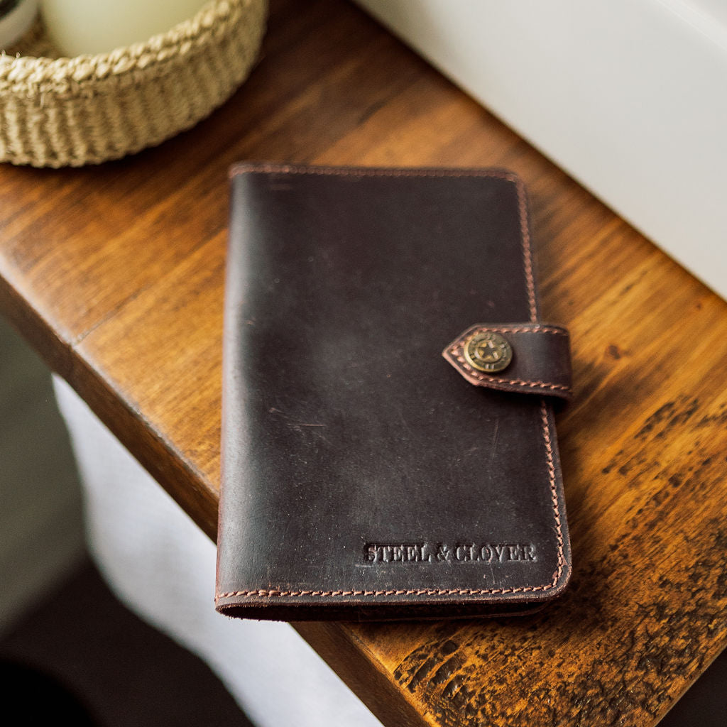Brown leather wallet with 'Steel & Clover' branding on a wooden surface