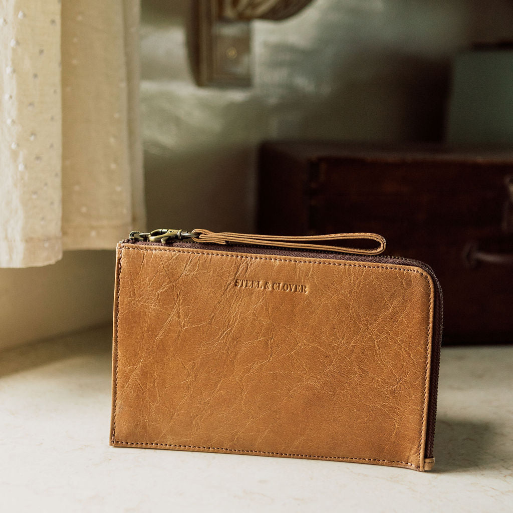 Brown leather wallet with 'Stella & Dot' branding on a surface with a blurred background