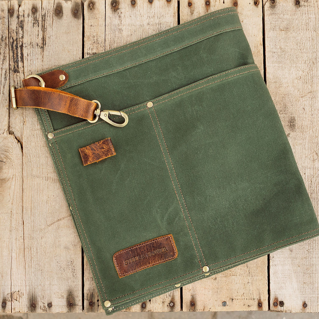 Green canvas apron with brown leather accents on a wooden surface