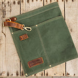 Green canvas apron with brown leather accents on a wooden surface
