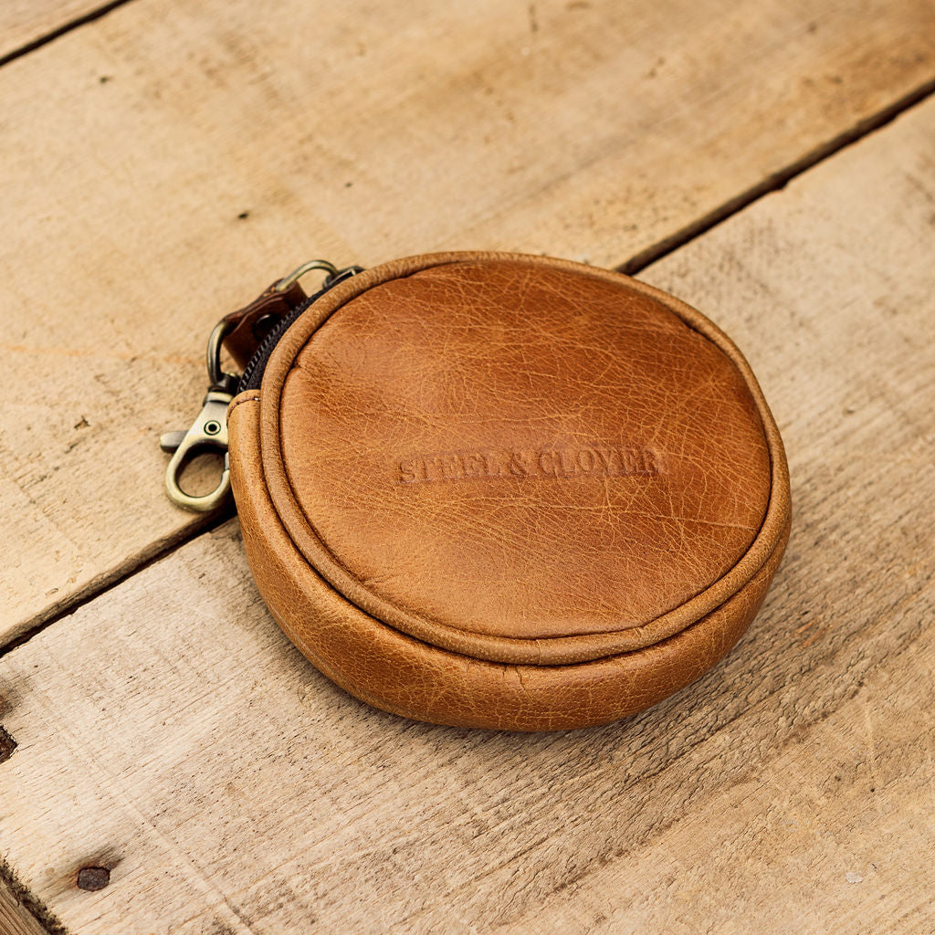 A collection of brown leather coin pouches with a brass lobster clasp, displayed on a wooden surface.