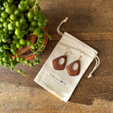 Wooden earrings on a drawstring bag with a plant on a wooden surface