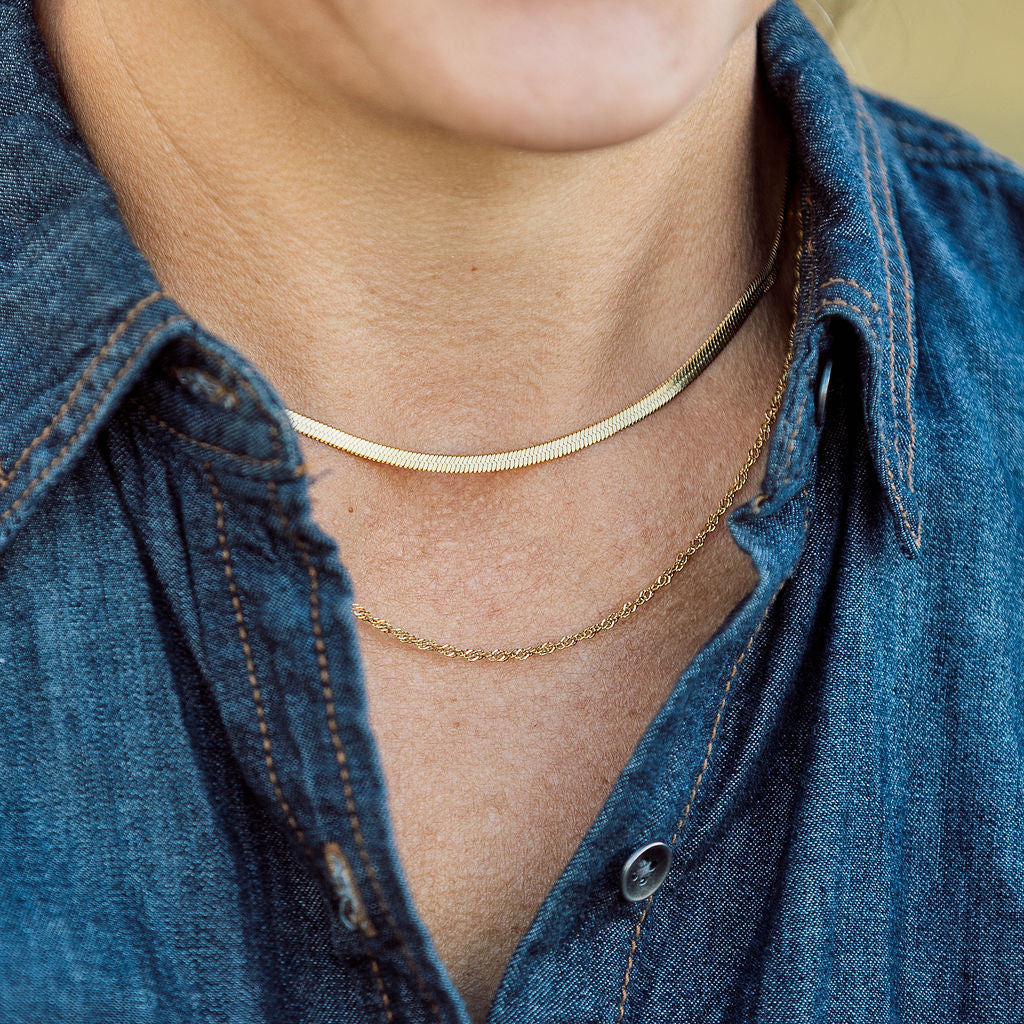 Person wearing a gold necklace with a blue denim shirt