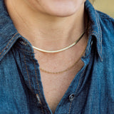 Person wearing a gold necklace with a blue denim shirt