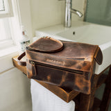 Brown leather toiletry bag on a bathroom counter with sink and window in the background