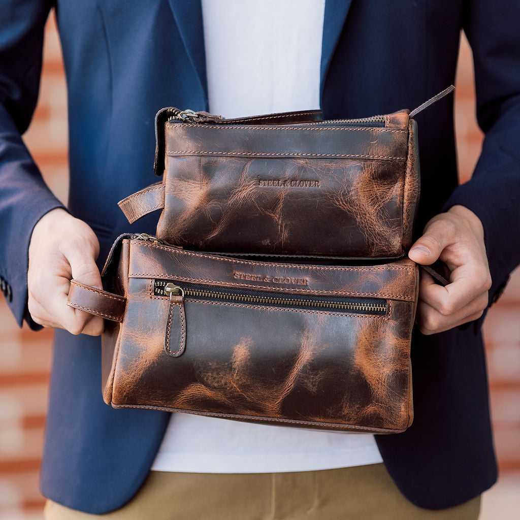 Brown leather clutch bag held by a person wearing a blue jacket.