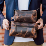 Brown leather clutch bag held by a person wearing a blue jacket.