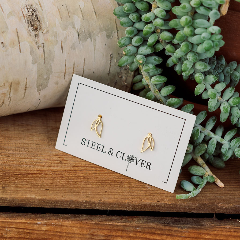 Gold earrings on a 'Steel & Clover' branded card with greenery in the background