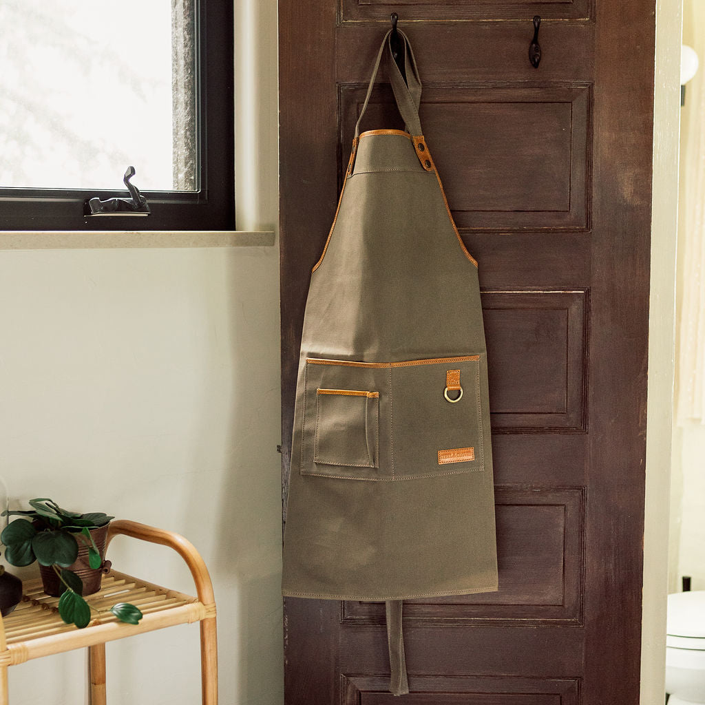 Green apron with brown accents hanging on a wooden door.