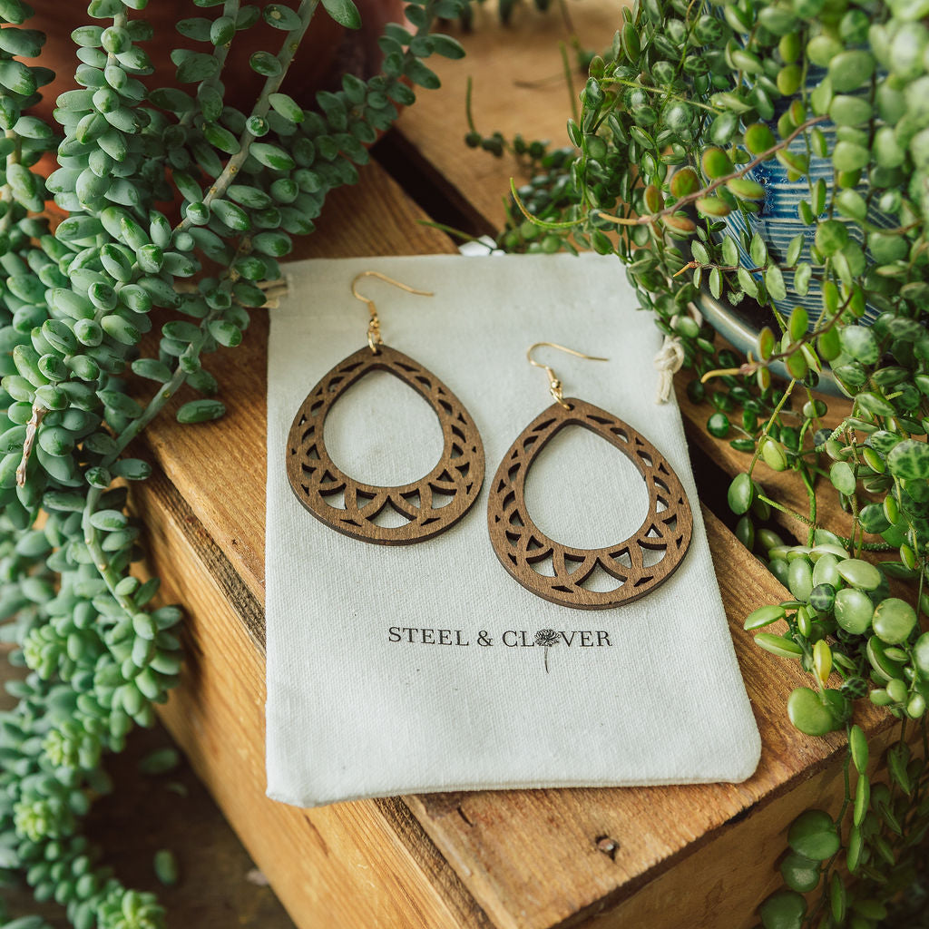 A pair of wooden hoop earrings with embossed detailing, displayed on a white card with the brand name 'Steel & Clover' visible.