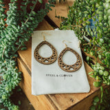 A pair of wooden hoop earrings with embossed detailing, displayed on a white card with the brand name 'Steel & Clover' visible.